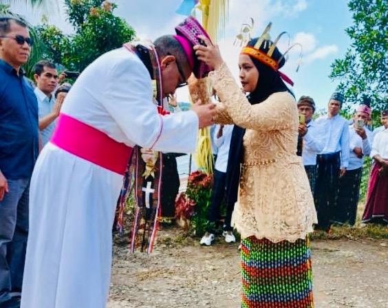 Siswi Muslim mengalungkan selendang dan topi pada Uskup Mgr. Maksi. (Foto : Tim KKI)